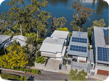 Aerial view of modern eco-friendly houses with solar panels near a lake, surrounded by lush greenery in a serene residential area.