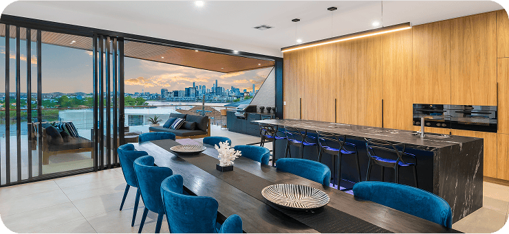 Luxury urban apartment with spacious open-plan living area, modern dining table, vibrant blue chairs, and panoramic city skyline view from large glass balcony doors.