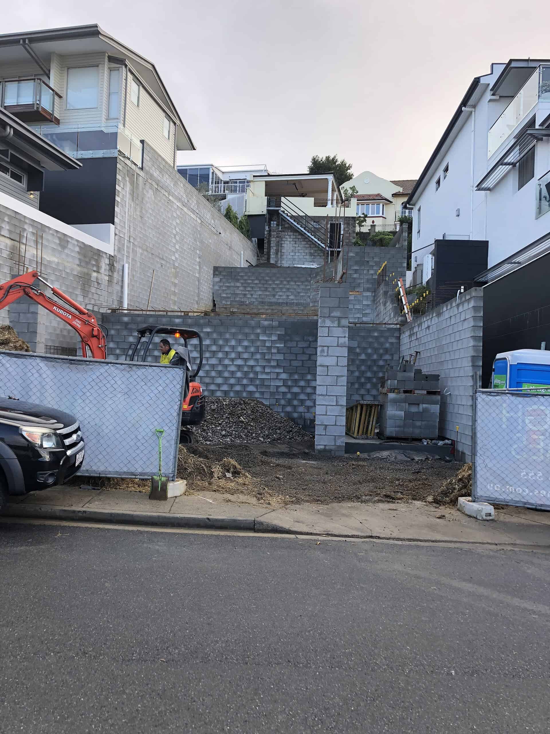 New construction in progress on a residential lot with construction equipment and unfinished retaining walls, showcasing a custom-built home project.