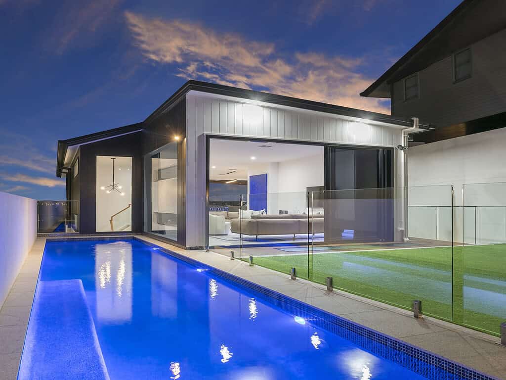Modern luxury house with illuminated pool and spacious living area, showcasing contemporary architecture and outdoor amenities for a luxurious lifestyle.