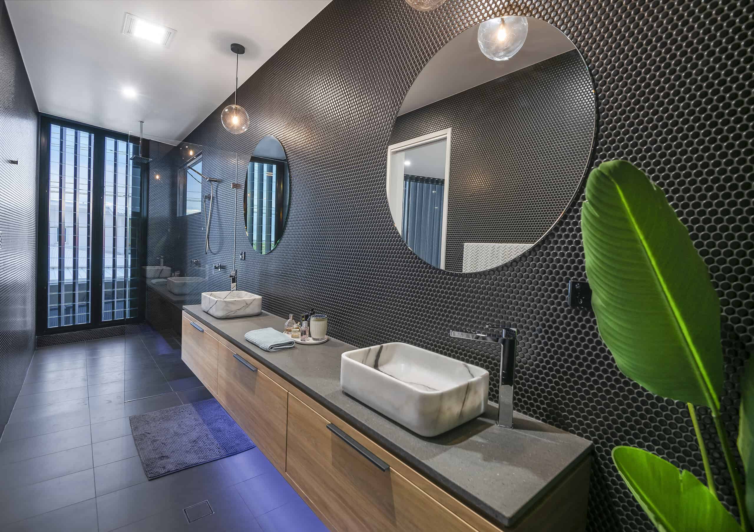 Sleek modern bathroom with black textured tile walls, large round mirrors, marble sinks, wooden cabinetry, and contemporary lighting, showcasing stylish interior design perfect for a website creator.
