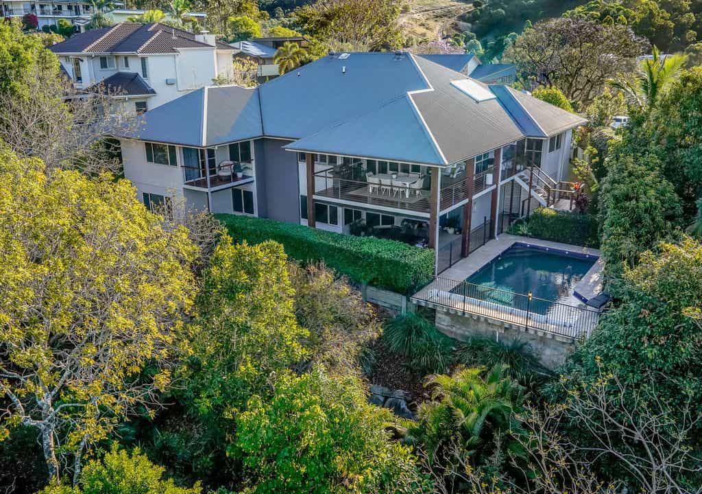 Modern two-storey house with a backyard pool, surrounded by lush greenery and trees, located in a hillside neighbourhood. Perfect for families seeking luxury living with outdoor entertaining options.
