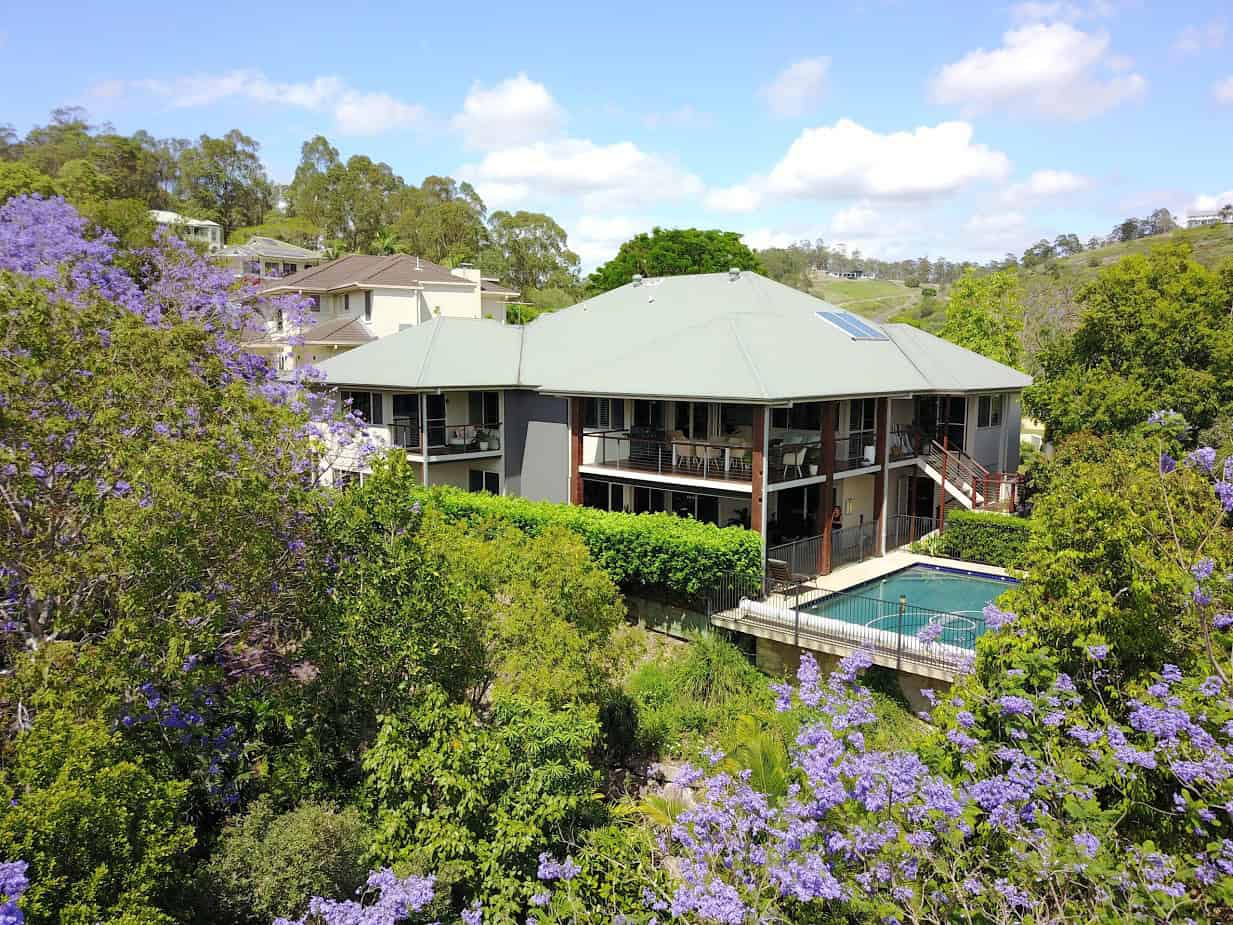 Modern hillside house with a swimming pool, surrounded by lush greenery and flowering trees, showcasing a beautiful outdoor space for relaxation and entertaining.