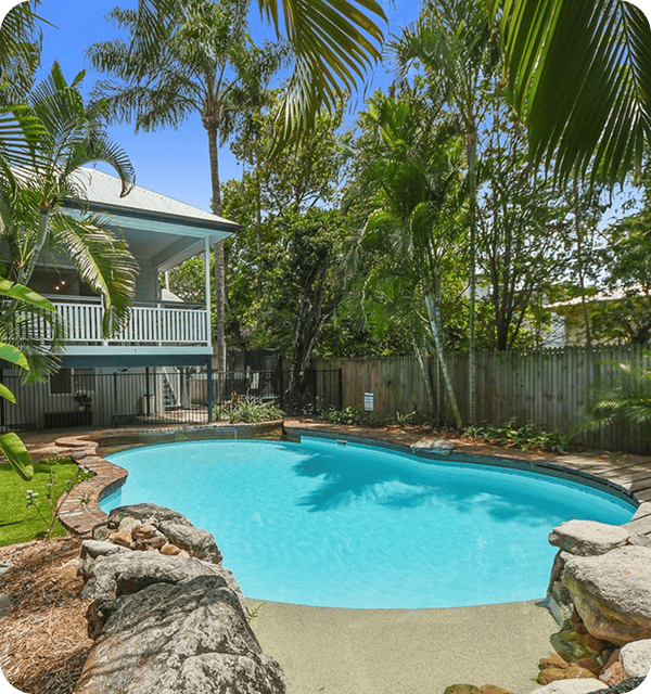 Pool and tropical garden in backyard with lush greenery and private fence, perfect for relaxation and outdoor activities. | A serene backyard featuring a swimming pool surrounded by tropical plants and a spacious deck, ideal for outdoor leisure. | This image showcases a beautifully designed backyard with a clear swimming pool, lush tropical plants, and a private fence, creating a perfect outdoor oasis for relaxation and entertaining guests. | Relevant to website creation for outdoor spaces, landscaping, and backyard design services.