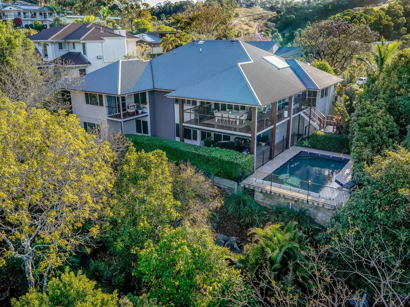 Modern multi-level home with a pool, surrounded by lush greenery, featuring expansive outdoor living areas, a garden, and scenic hill views, ideal for luxury lifestyle and relaxation.