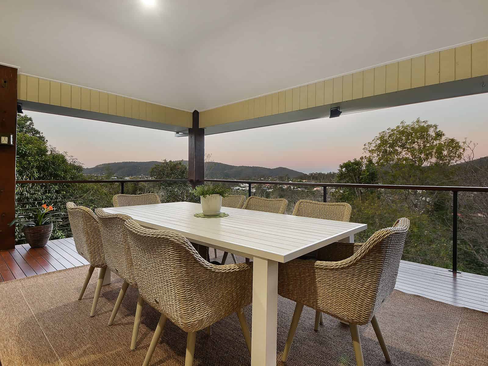 Modern outdoor terrace with a white dining table and woven chairs overlooking scenic landscapes, perfect for hosting gatherings.