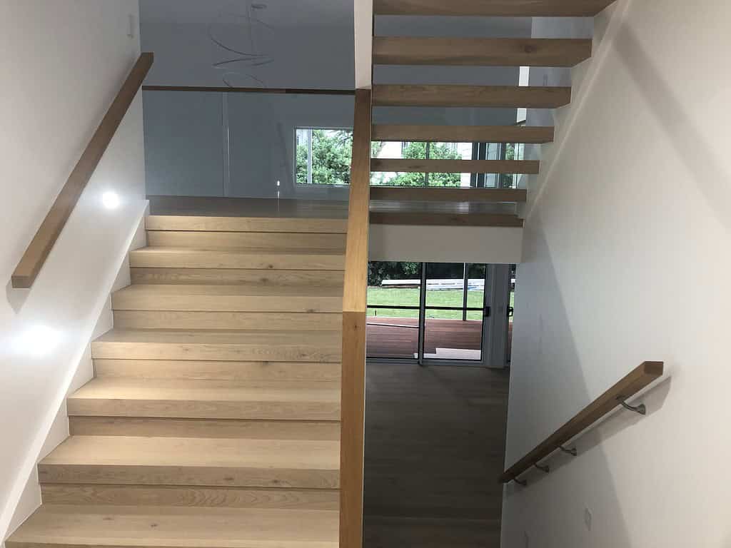 Modern wooden staircase inside a new home with natural light and glass sliding doors, showcasing contemporary interior design and craftsmanship, perfect for residential construction in Australia.