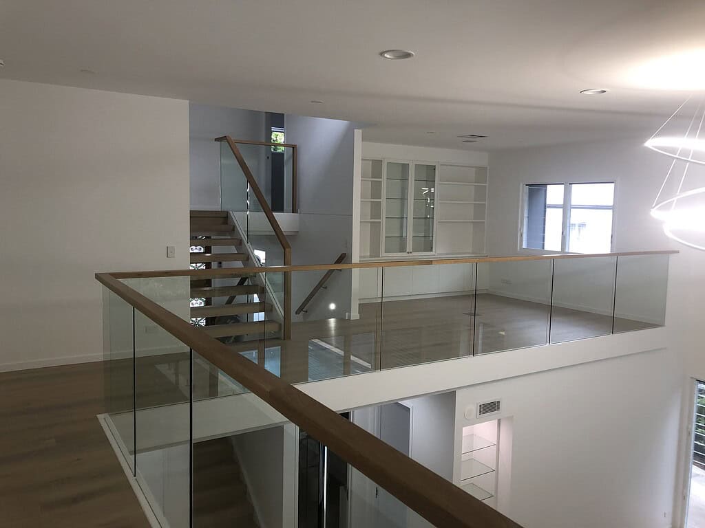 Modern interior of a newly built home showcasing an open-plan staircase, glass balustrades, and minimalist white cabinetry, highlighting contemporary Australian residential design.